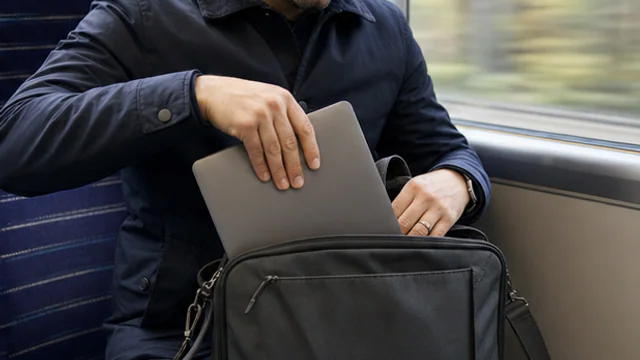 Commuter checking that an unbranded laptop fits inside a work bag on a train.