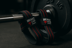 Close-up of Beast Gear GelGrip lifting straps wrapped around a knurled 20 kg Olympic barbell in a dim-lit power-lifting gym.